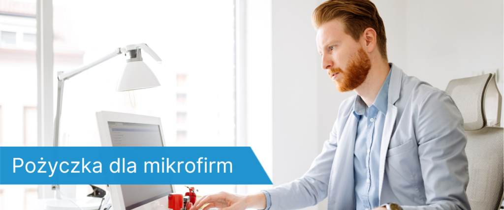 Skoncentrowany mężczyzna z brodą, siedzący przy biurku i pracujący na komputerze