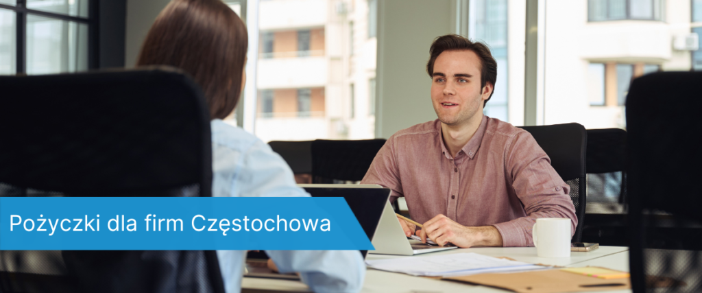 Dwóch młodych mężczyzn rozmawia przy biurku w jasnym biurze z widokiem na miasto